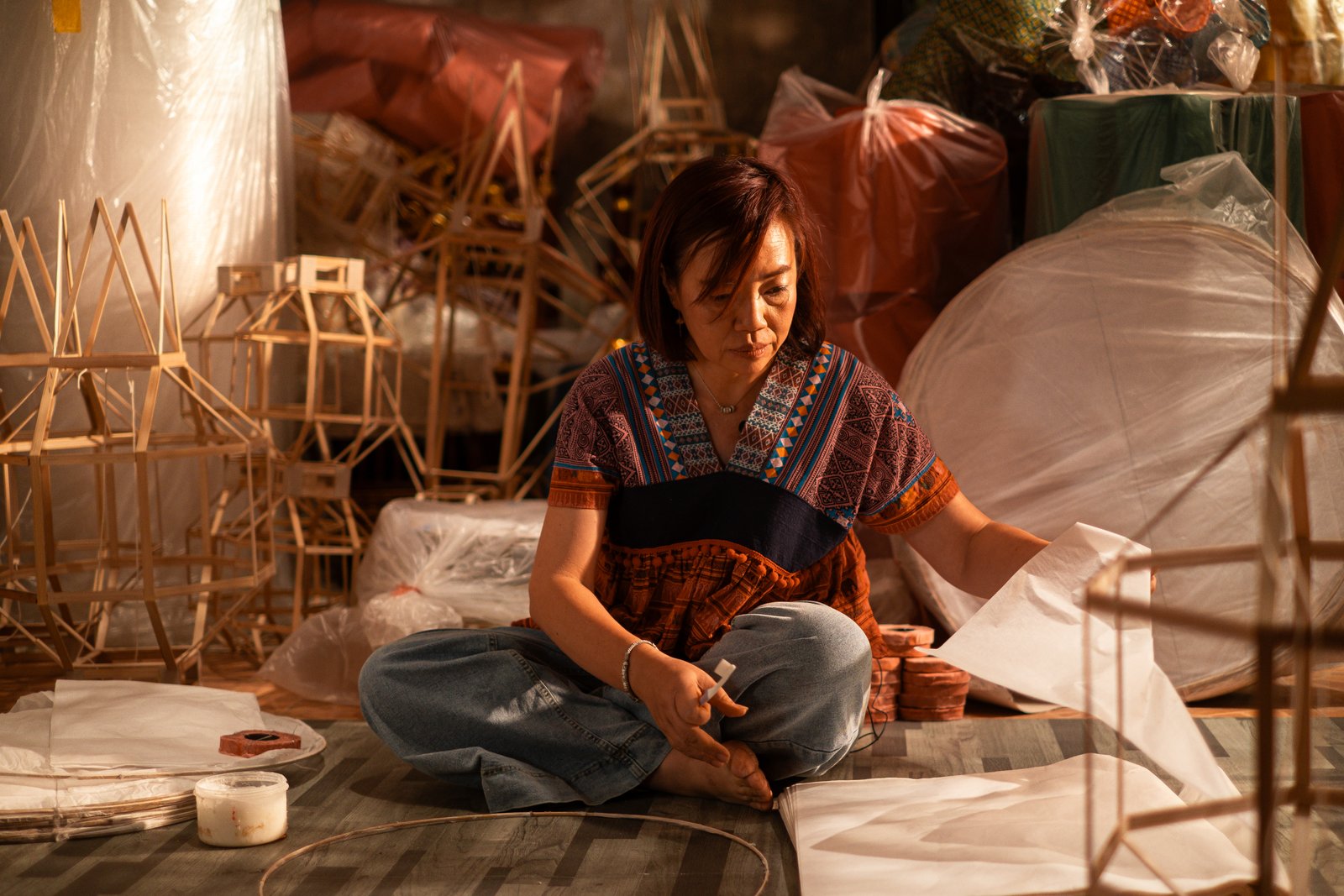 A hill tribe woman seated with a huge round paper lantern shade in warm light