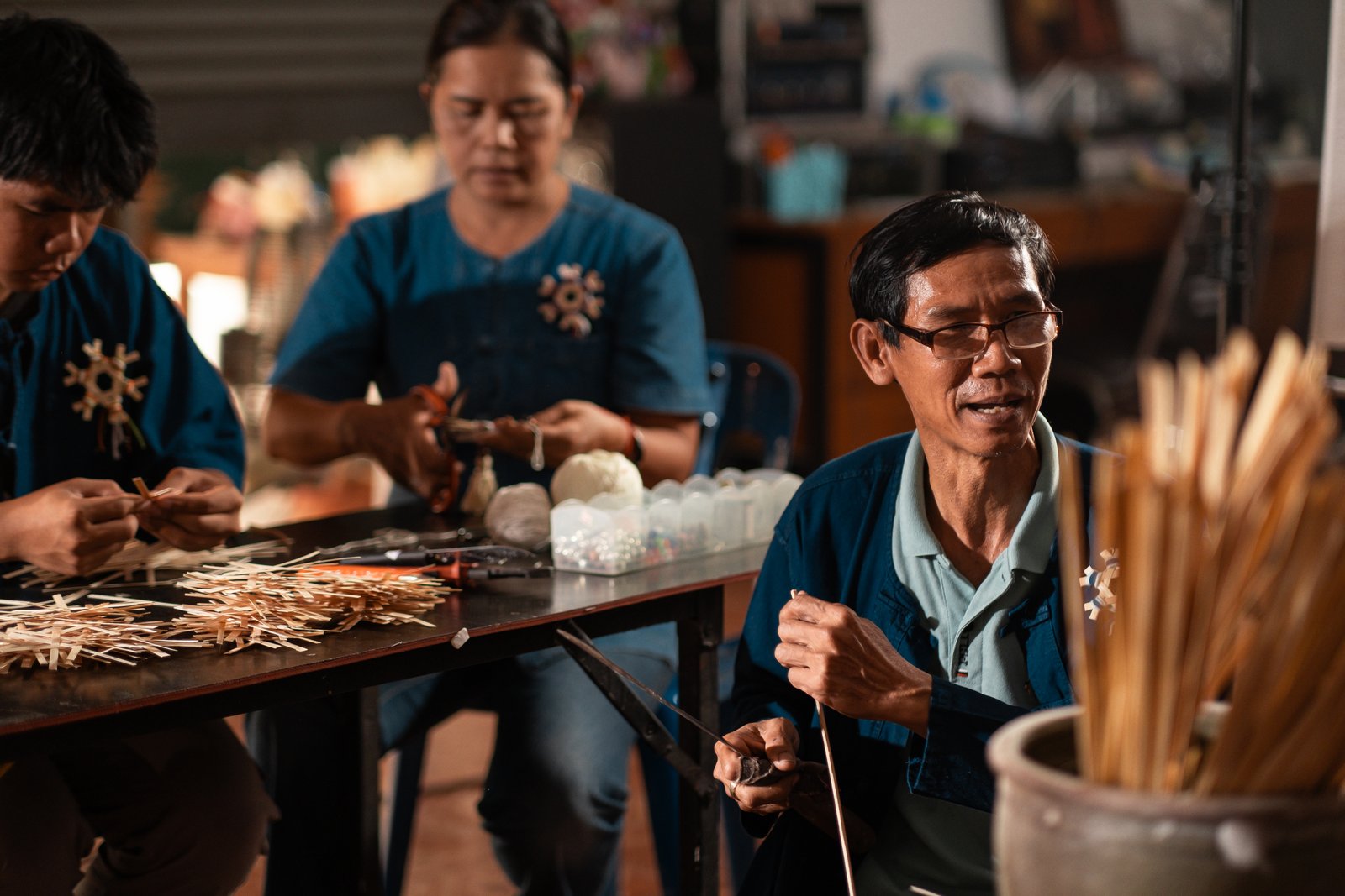 Two garland makers working at a table in warm lamplight