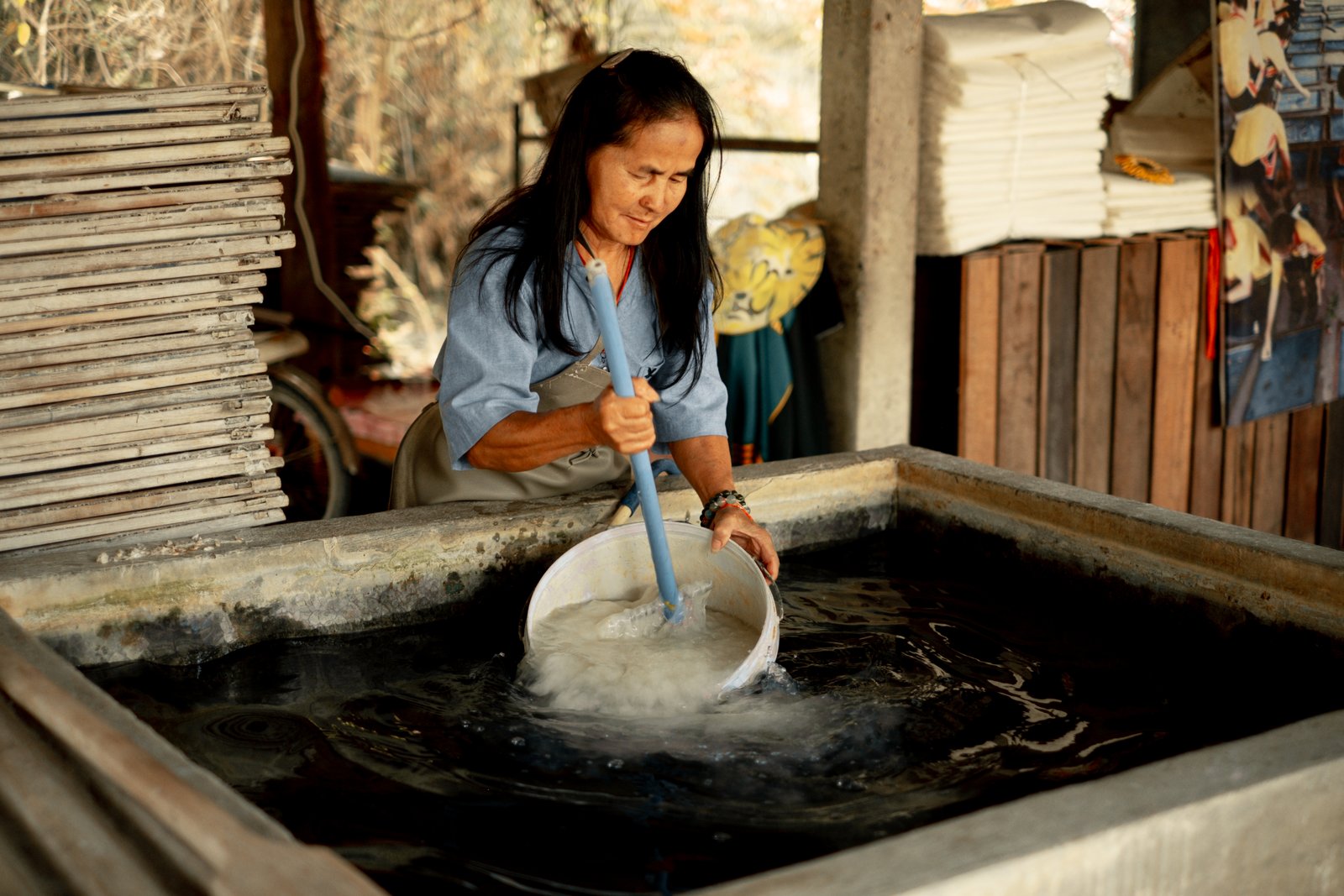 A woman lifting saa paper pulp from a stone vat