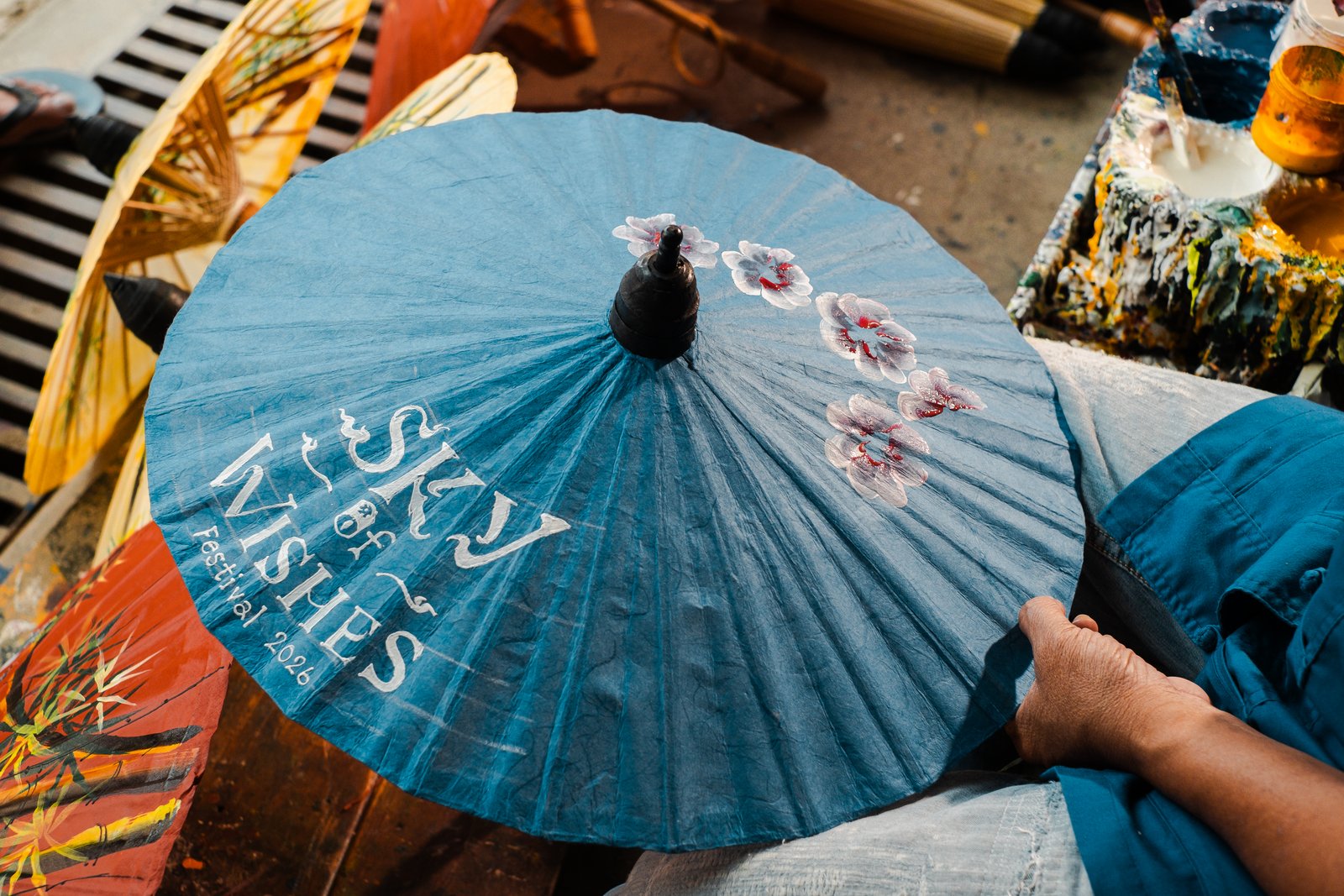 A blue Sky of Wishes umbrella being painted, wide workshop scene